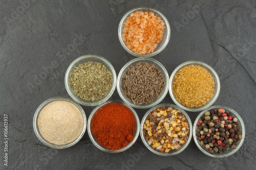 Various kinds of spices in glass bowls on a slate background. Preparation for cooking spicy food. Spices for master cook. The spice trade. Sale of spices in the kitchen.
