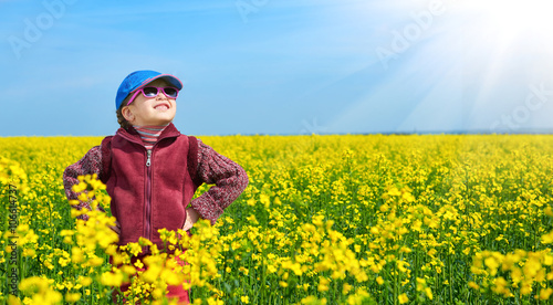 girl child in rapeseed field with bright yellow flowers, spring landscape