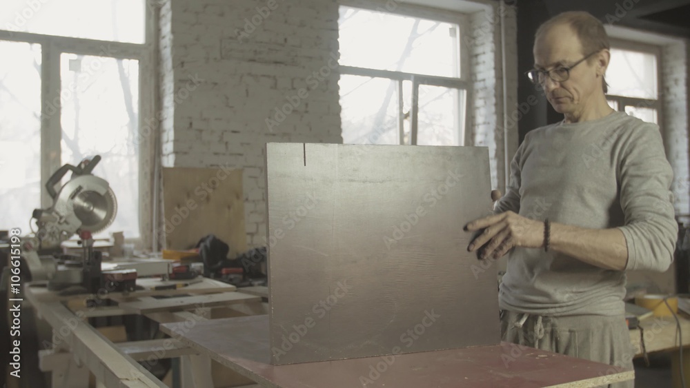 Professional adult carpenter connects two equal wooden boards on working table. Process of making furniture. Professional adult carpenter connects two equal wooden boards on working table. Process of making furniture.