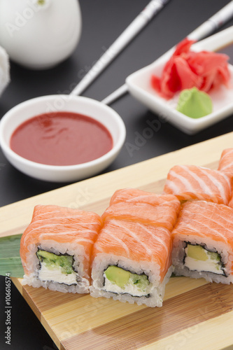 Salmon sushi roll on wooden plate ( gete ) with ginger wasabi chopsticks and sauces over black background