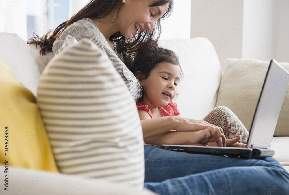 Hispanic mother and daughter using laptop on sofa Hispanic mother and daughter using laptop on sofa