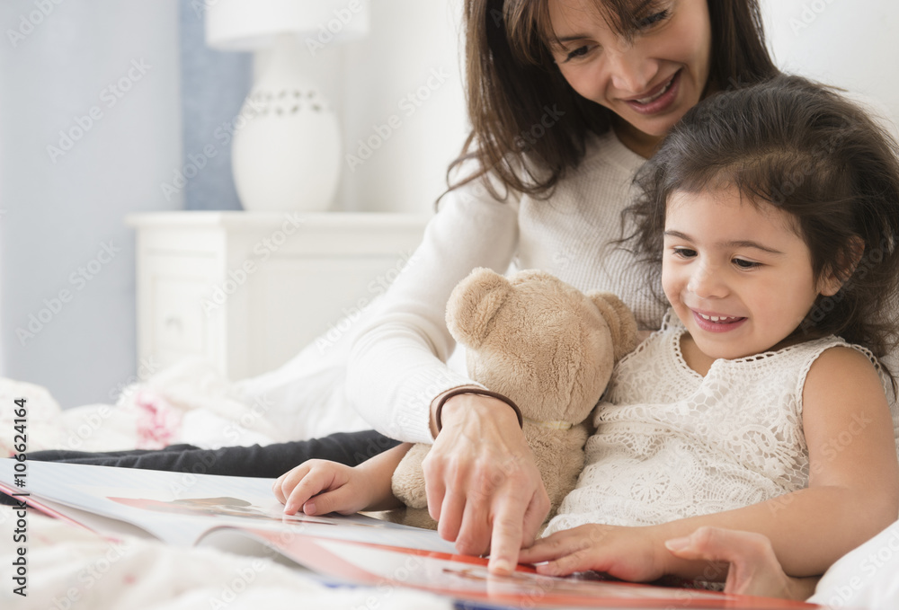 Hispanic mother and daughter reading in bed Hispanic mother and daughter reading in bed