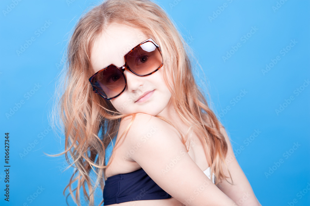 Cute baby girl wearing sun glasses on blue background