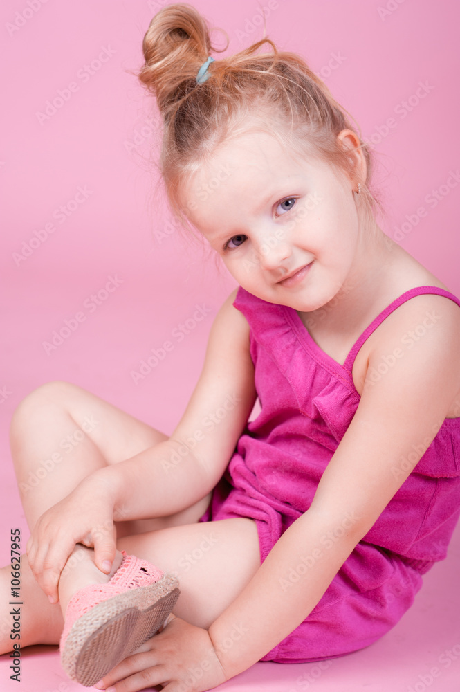 Smiling blonde girl wearing summer clothes in room. Siting on floor over pink. Summer time. Smiling blonde girl wearing summer clothes in room. Siting on floor over pink. Summer time.