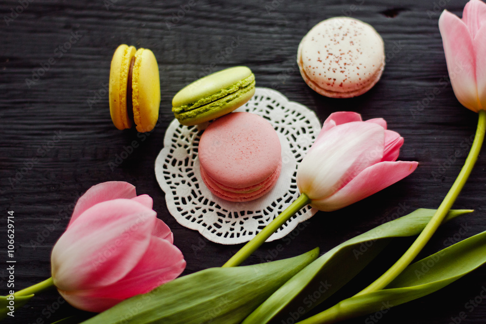 A beautiful flowers pink tulips with colorful macaroons laid on dark wooden background with Lacy napkin A beautiful flowers pink tulips with colorful macaroons laid on dark wooden background with Lacy napkin