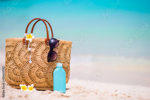 Beach accessories - straw bag, headphones, bottle of cream and sunglasses on the beach