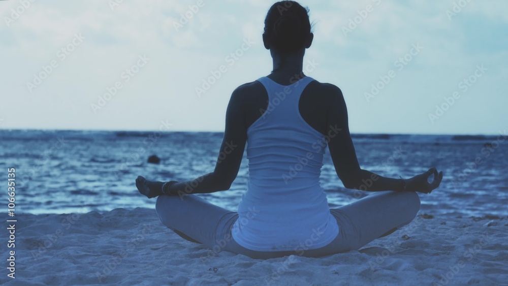 Woman sitting in yoga lotus pose on the caribbean beach at dawn ...
