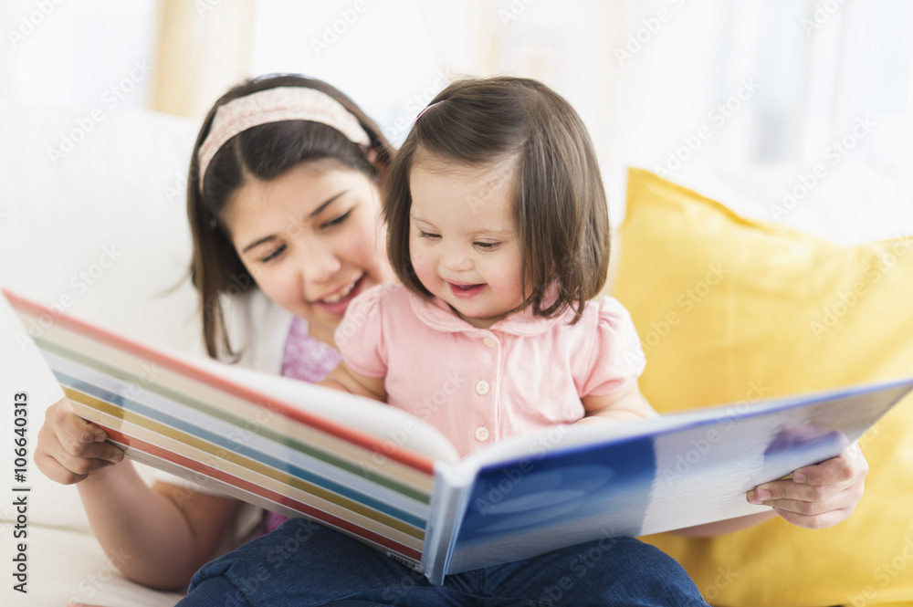 Hispanic girl reading to toddler sister in living room Hispanic girl reading to toddler sister in living room