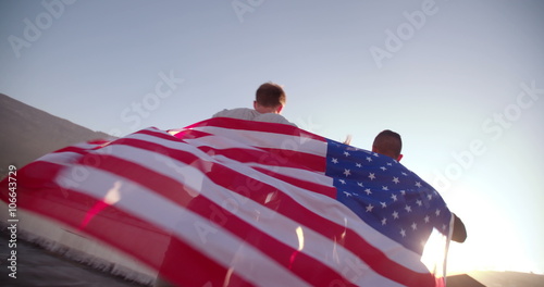 Friends holding American flag over shoulders on roftop photo