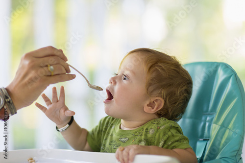 Caucasian mother feeding baby in high chair photo