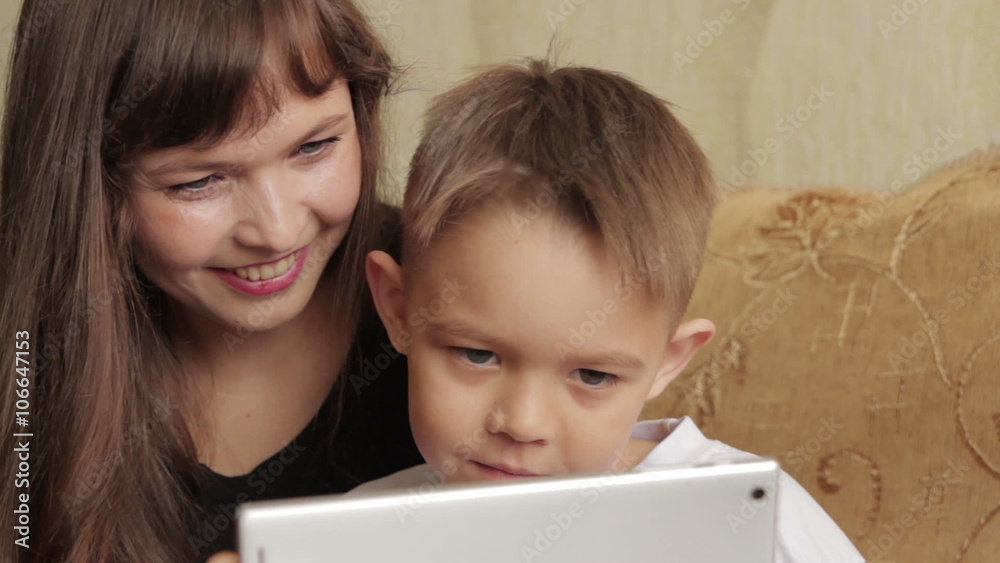 Cheerful little boy and his mother sitting on the couch using a digital tablet Cheerful little boy and his mother sitting on the couch using a digital tablet