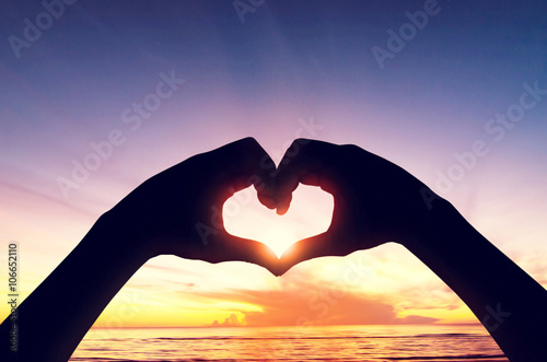 Valentine's day concept, Silhouette (Focused) hand in heart shape with sunset in the middle and sea (Blurred) background