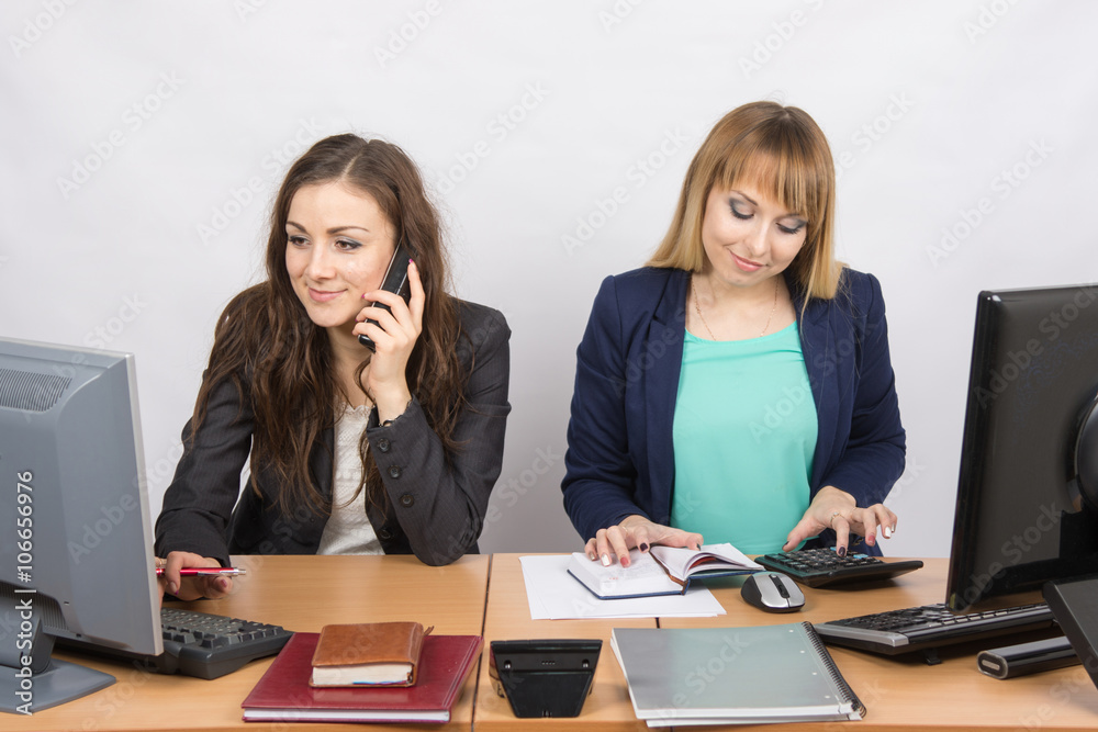 Office colleagues girl sitting behind a desk, with a phone, the other with a calculator Office colleagues girl sitting behind a desk, with a phone, the other with a calculator
