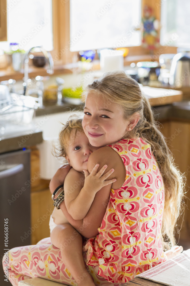 Caucasian girl holding toddler brother in kitchen Caucasian girl holding toddler brother in kitchen