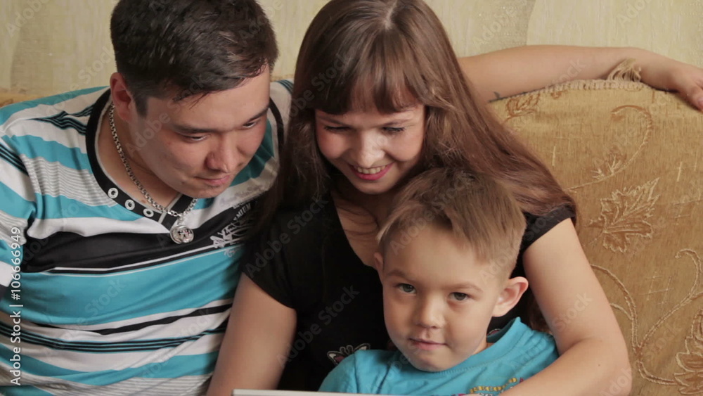 Cheerful little boy and his parents sitting on sofa while using digital tablet Cheerful little boy and his parents sitting on sofa while using digital tablet