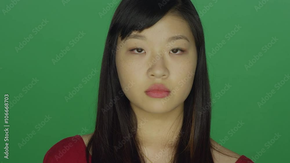 Young Asian woman staring and looking serious, on a green screen studio background Young Asian woman staring and looking serious, on a green screen studio background