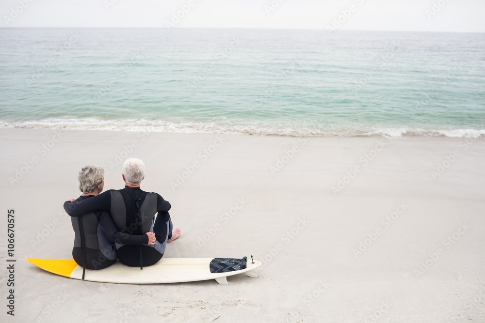 Rear view of couple sitting on surfboard 