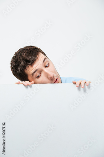 Young man peeking from blank board photo