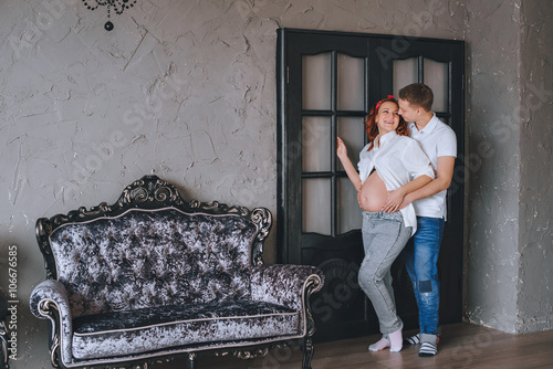 Joyful young man and a beautiful pregnant woman hugging each other.  We look at each other and hug the midsection. Fashion photoshoot in the Studio. A woman in jeans and a white shirt.