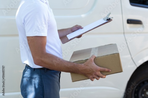 Midsection of delivery man with clipboard and cardboard box 