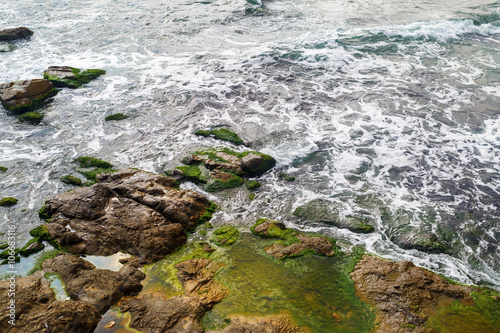 Close-up of sea surf. Shore with sea water and large rocks covered with algae. Rocky coastline with sea water and boulders. © Veresovich