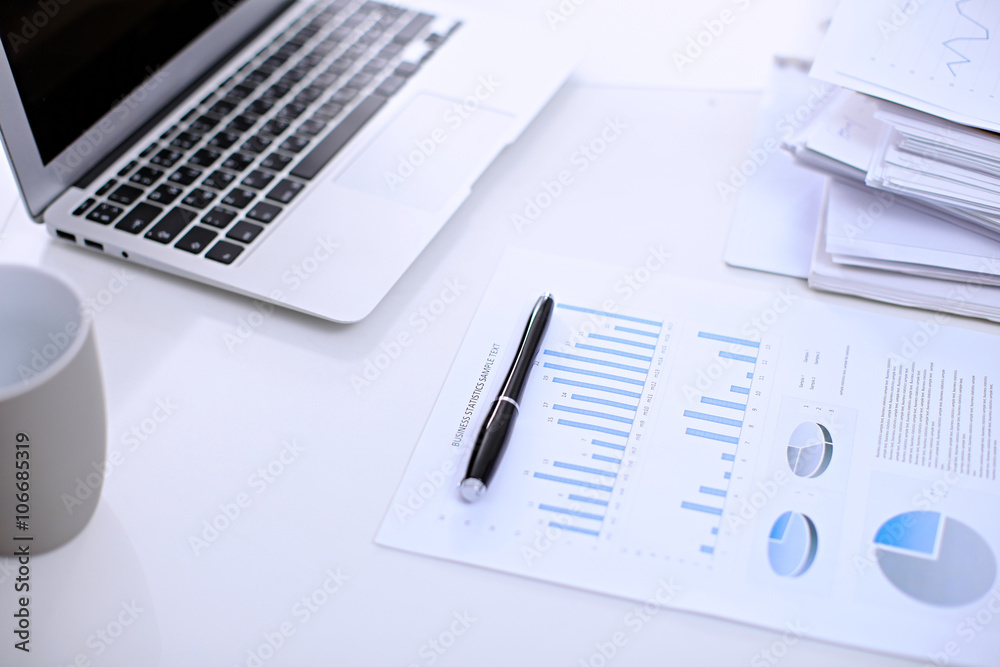 .Office workplace with a laptop and financial documents on the light reflecting table .Office workplace with a laptop and financial documents on the light reflecting table