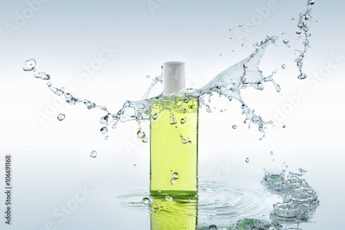 The  green herbal  moisturizing shampoo stands on the water background with big blue splash above the bottle