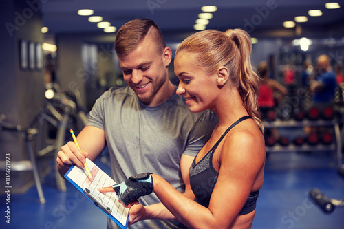 smiling woman with trainer and clipboard in gym