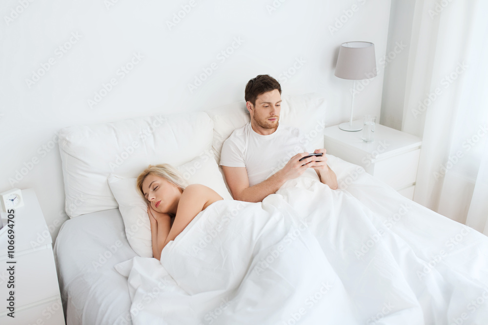 Fototapeta premium man texting message while woman is sleeping in bed