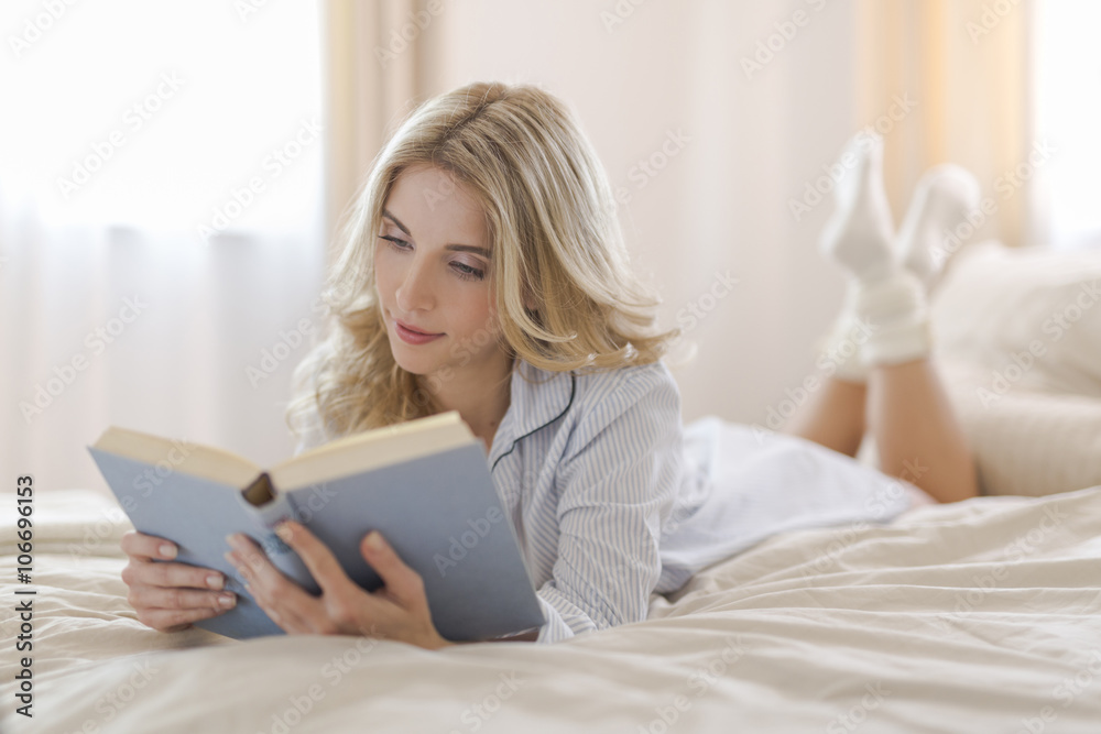 Portrait of blond woman lying on bed reading a book Portrait of blond woman lying on bed reading a book