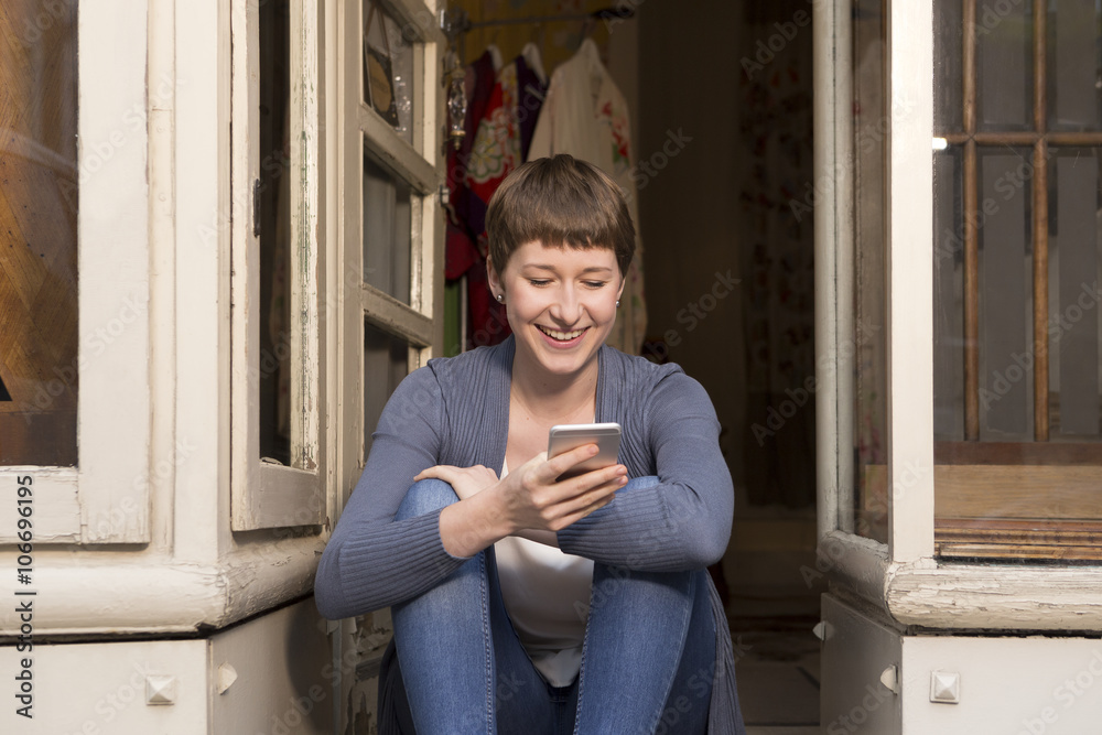 Portrait of female fashion designer with smartphone sitting at the entrance of her studio Portrait of female fashion designer with smartphone sitting at the entrance of her studio
