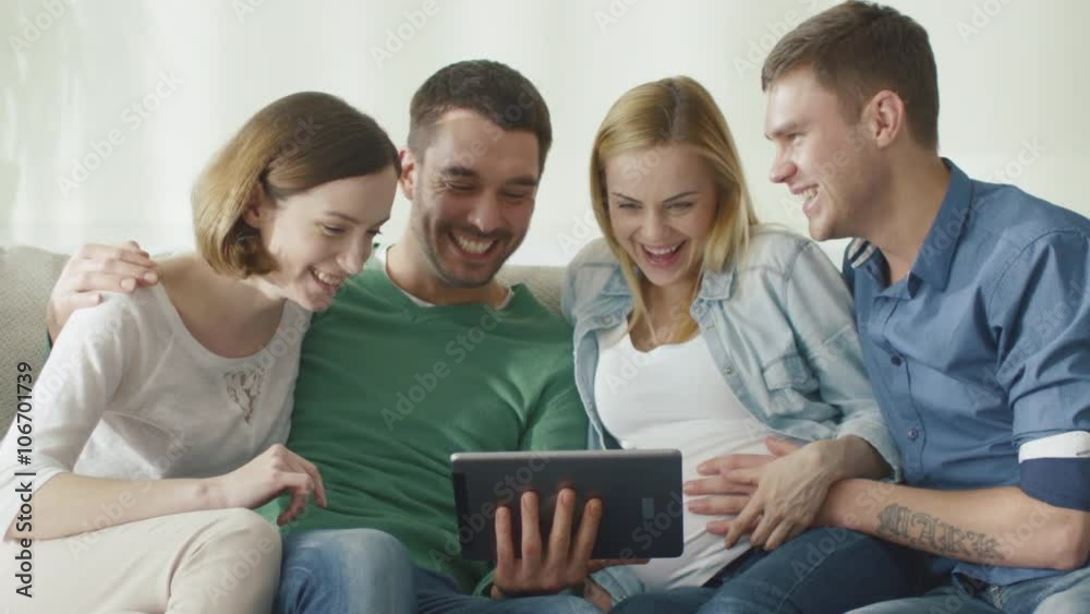 Friends are sitting on the couch at home and using tablet for entertainment. Shot on RED Cinema Camera. Friends are sitting on the couch at home and using tablet for entertainment. Shot on RED Cinema Camera.