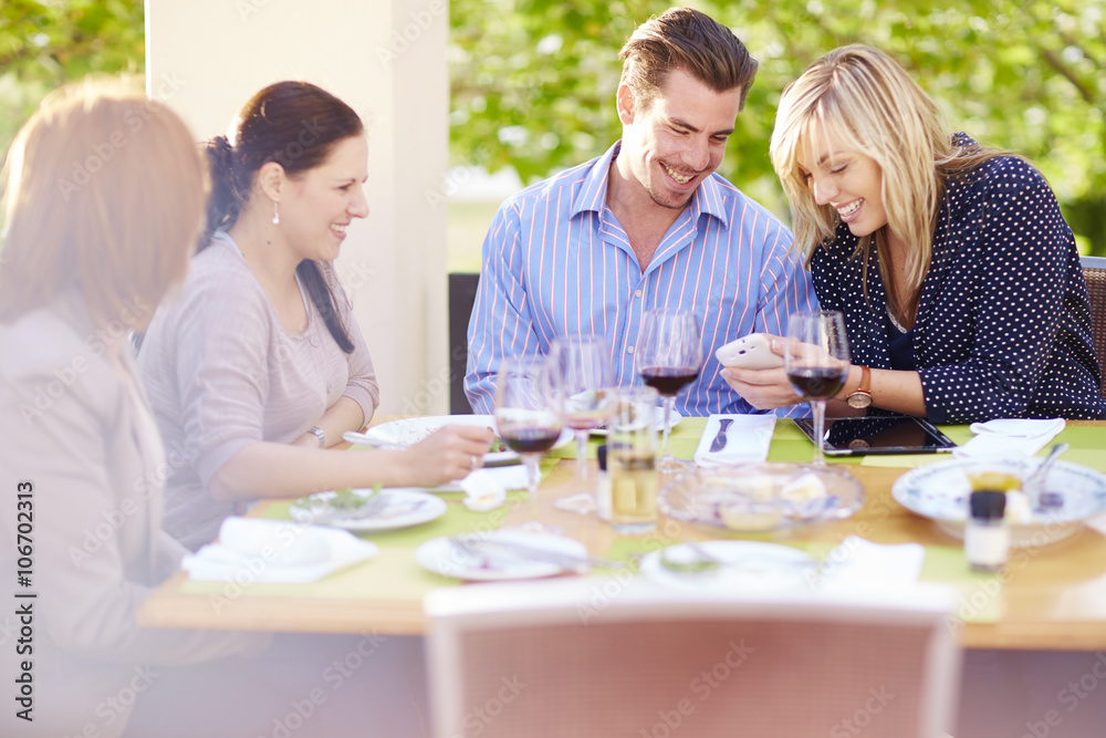 Woman showing cell phone to friends at dining table Woman showing cell phone to friends at dining table