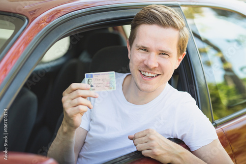Junger Mann sitzt im Auto und zeigt seinen Führerschein