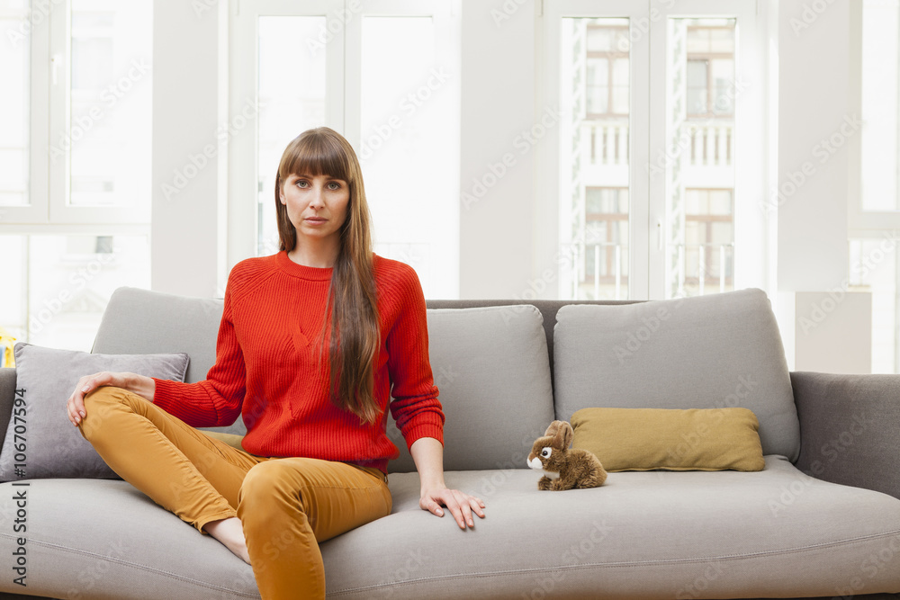 Serious woman sitting on sofa next to cuddly toy