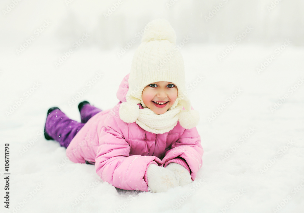 Happy smiling little girl child lying on snow in winter day