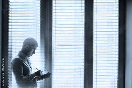 businessman near the window with blinds writing in a notebook