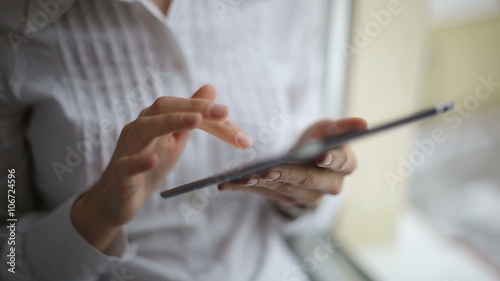 Woman at a window scrolling through her tablet