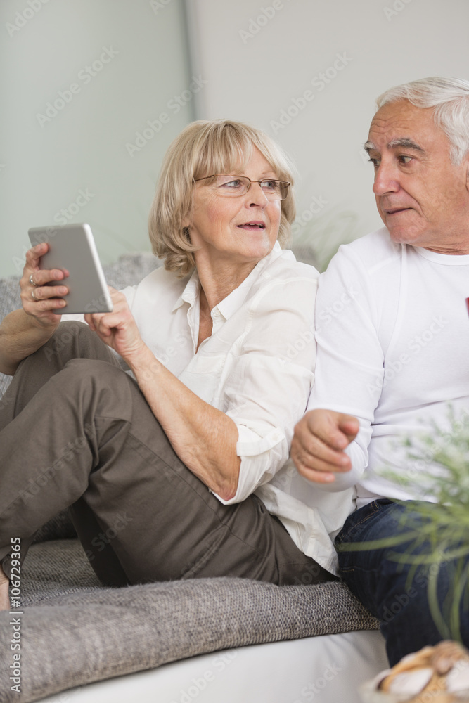 Senior couple with digital tablet side by side on sofa in living room Senior couple with digital tablet side by side on sofa in living room