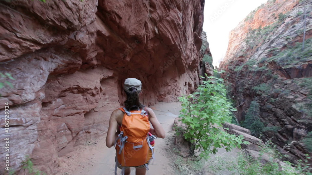Hiking woman on hike in Zion National Park. Happy woman hiker trekking on walking path in Zion Canyon wearing backpack. Healthy lifestyle image with multiracial Asian Caucasian girl in Utah, USA.