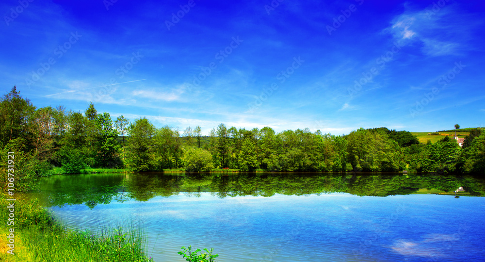  Lake and green trees on sky background.