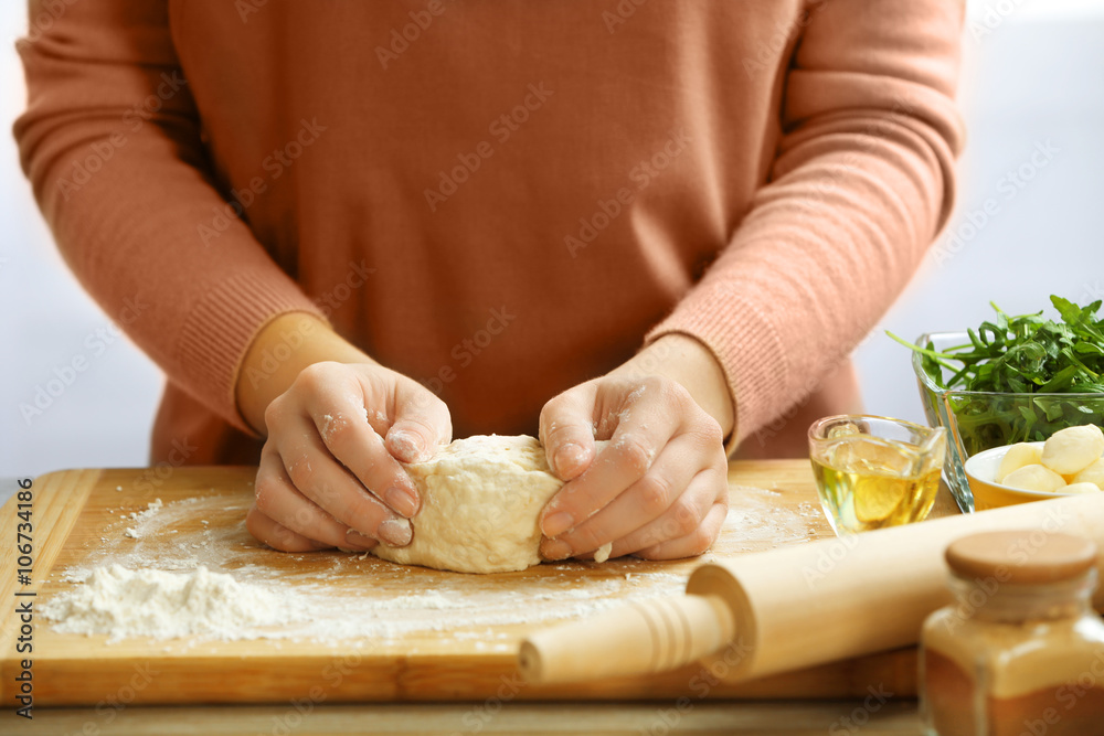 Woman making a pizza dough on a wooden board, close up