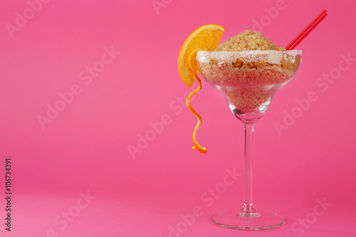 Margarita glass with brown sugar, cocktail straw and orange slice on pink background
