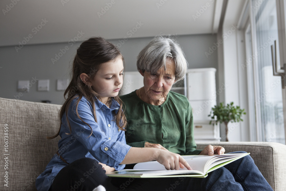 Grandmother and granddaughter reading book on sofa