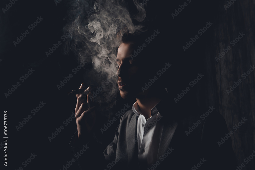 Attractive young man with cigar and smoke on black background