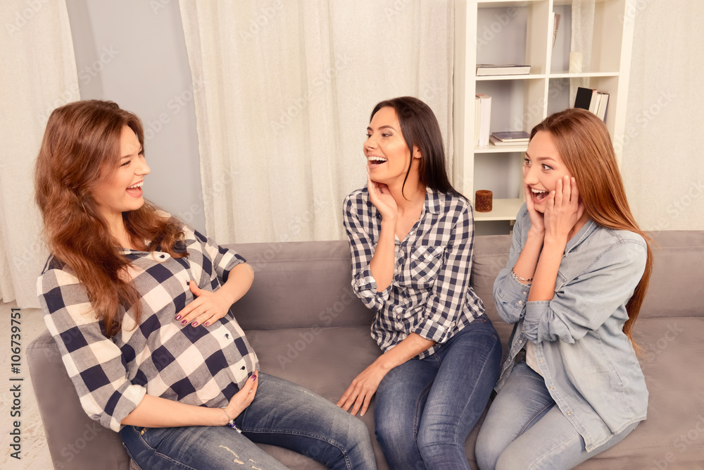 Pregnant woman and her friends sitting on sofa and laughing Pregnant woman and her friends sitting on sofa and laughing