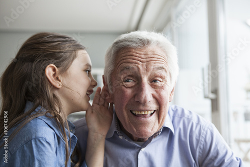 Granddaughter whispering something in the ear of her grandfather photo