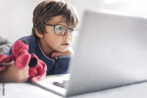 Portrait of little boy wearing oversized glasses looking at laptop photo