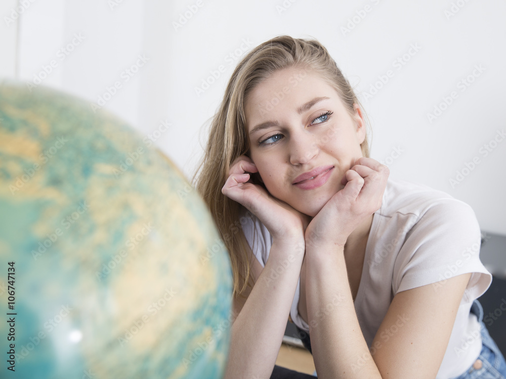 Portrait of daydreaming young woman with head in her hands besides a globe Portrait of daydreaming young woman with head in her hands besides a globe