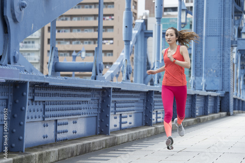 Young woman is running wearing sportswear on the bridge